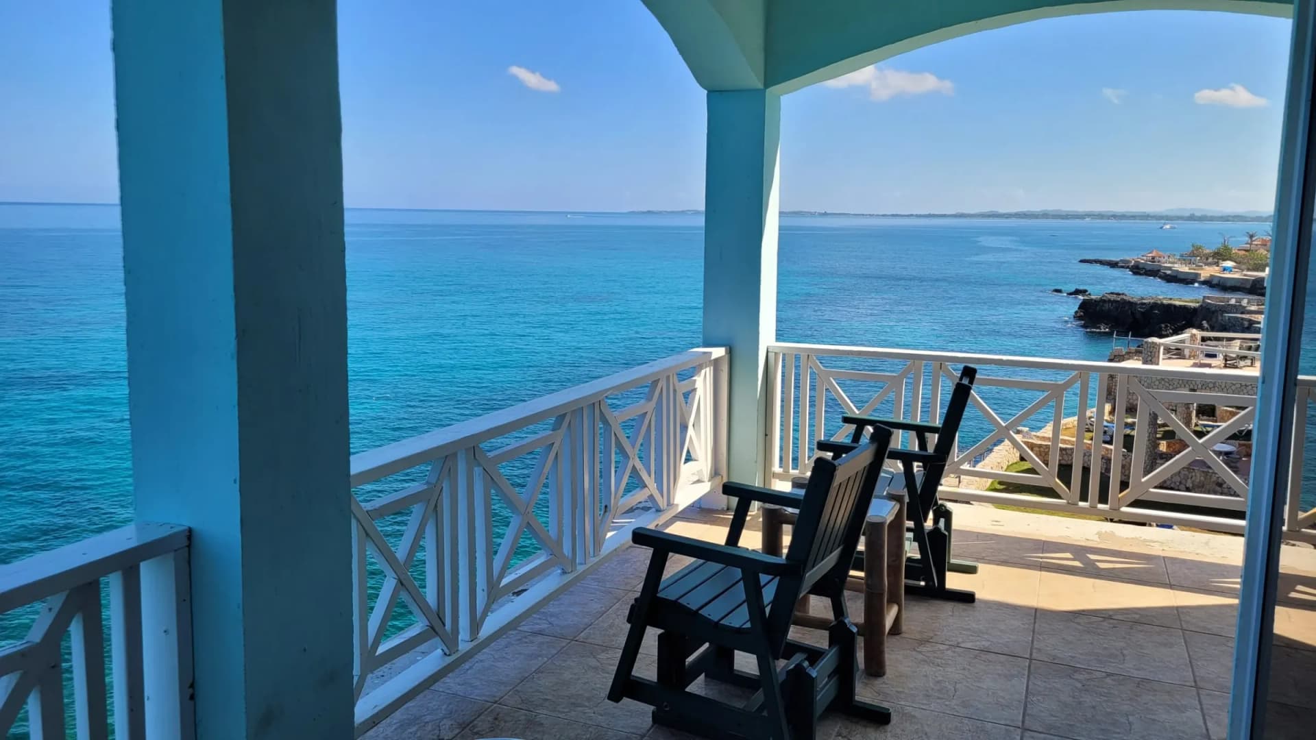 Two wooden chairs on a covered balcony over the Caribbean Sea, the West End coast beyond
