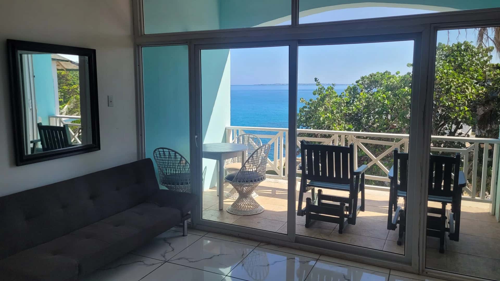 Open living area with a sofa opening through sliding glass doors to a private sea-view balcony in the Two Bedroom Suite, Room 18