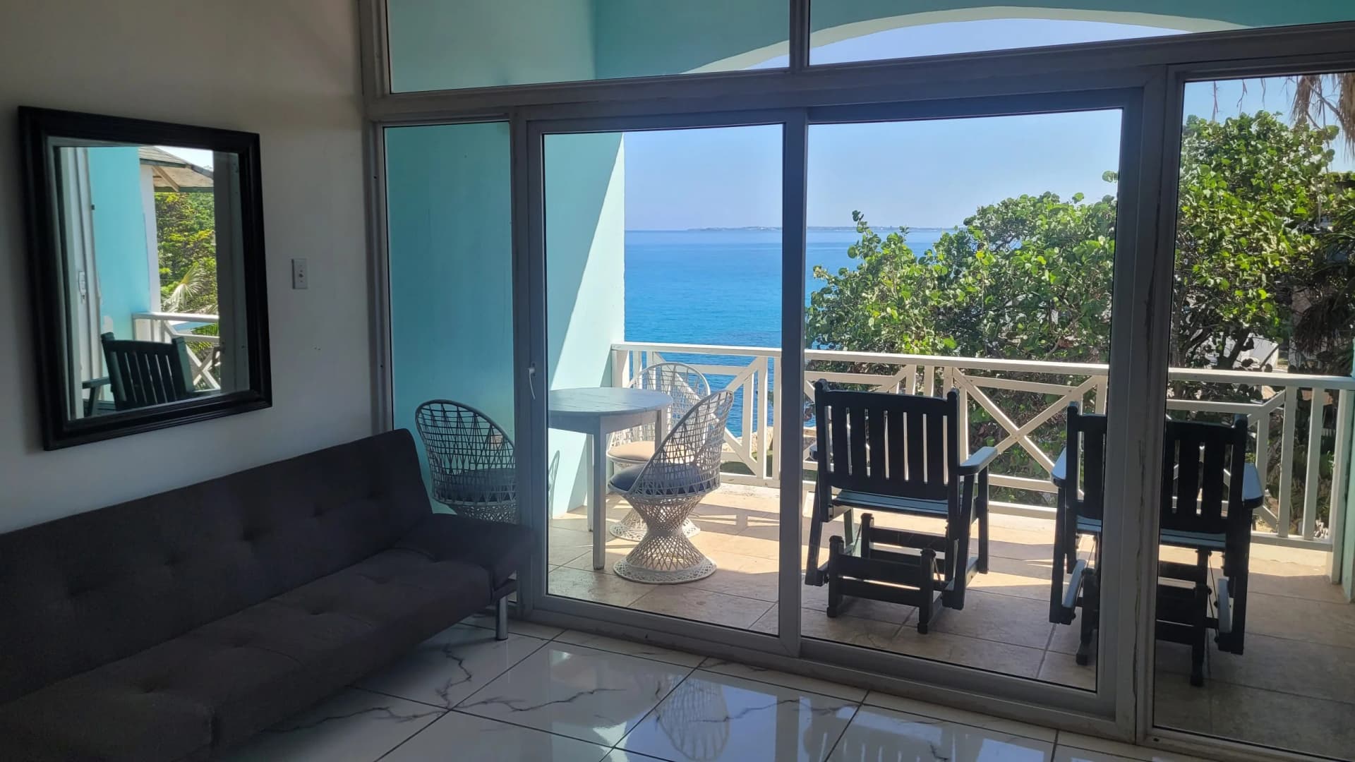 Open living area with a sofa opening through sliding glass doors to a private sea-view balcony in the Two Bedroom Suite, Room 18